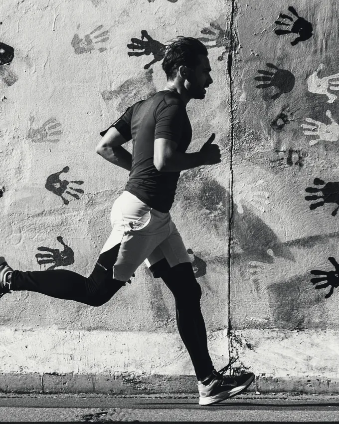 Un coureur en tee-shirt technique longe un mur couvert d’empreintes de mains.