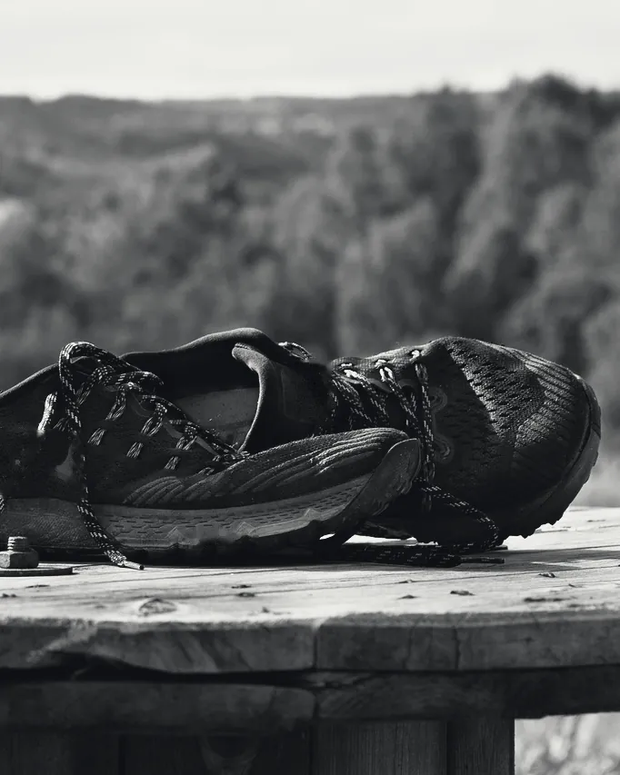 Chaussures de trail noires posées sur une table en bois, en forêt.