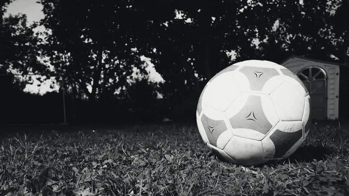 Un ballon de football posé sur l’herbe, à la tombée de la nuit.